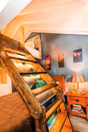 A wooden spiral staircase with a view of the room below, a small wooden table with a lamp, and wall-mounted pictures.
