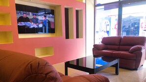 Una sala de estar con un sofá rojo, una mesa de centro de vidrio y un televisor montado en una pared rosa.
