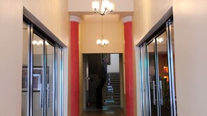 Un pasillo con puertas de cristal a ambos lados, un candelabro y una escalera al fondo.