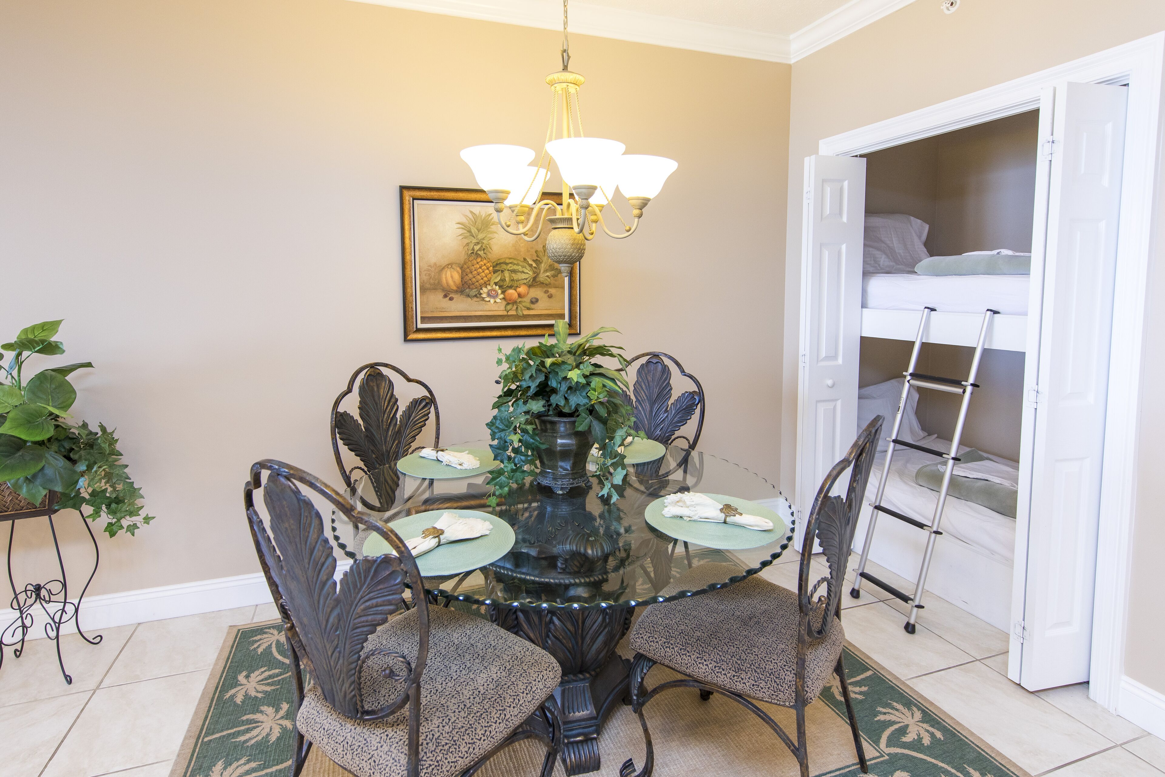 A dining area with a glass table, metal chairs, a chandelier, and a painting on the wall.