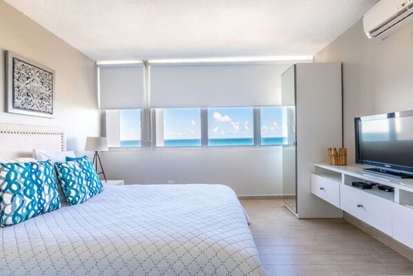 Quarto moderno com cama grande, televisão e vista para o mar.