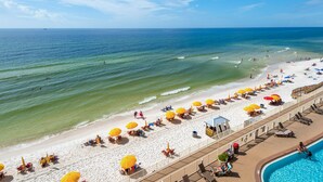 Ein Strand mit weißem Sand, klarem blauen Wasser und gelben Sonnenschirmen.