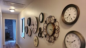 Un pasillo con varios relojes en la pared, piso de madera y una puerta que da a otra habitación.