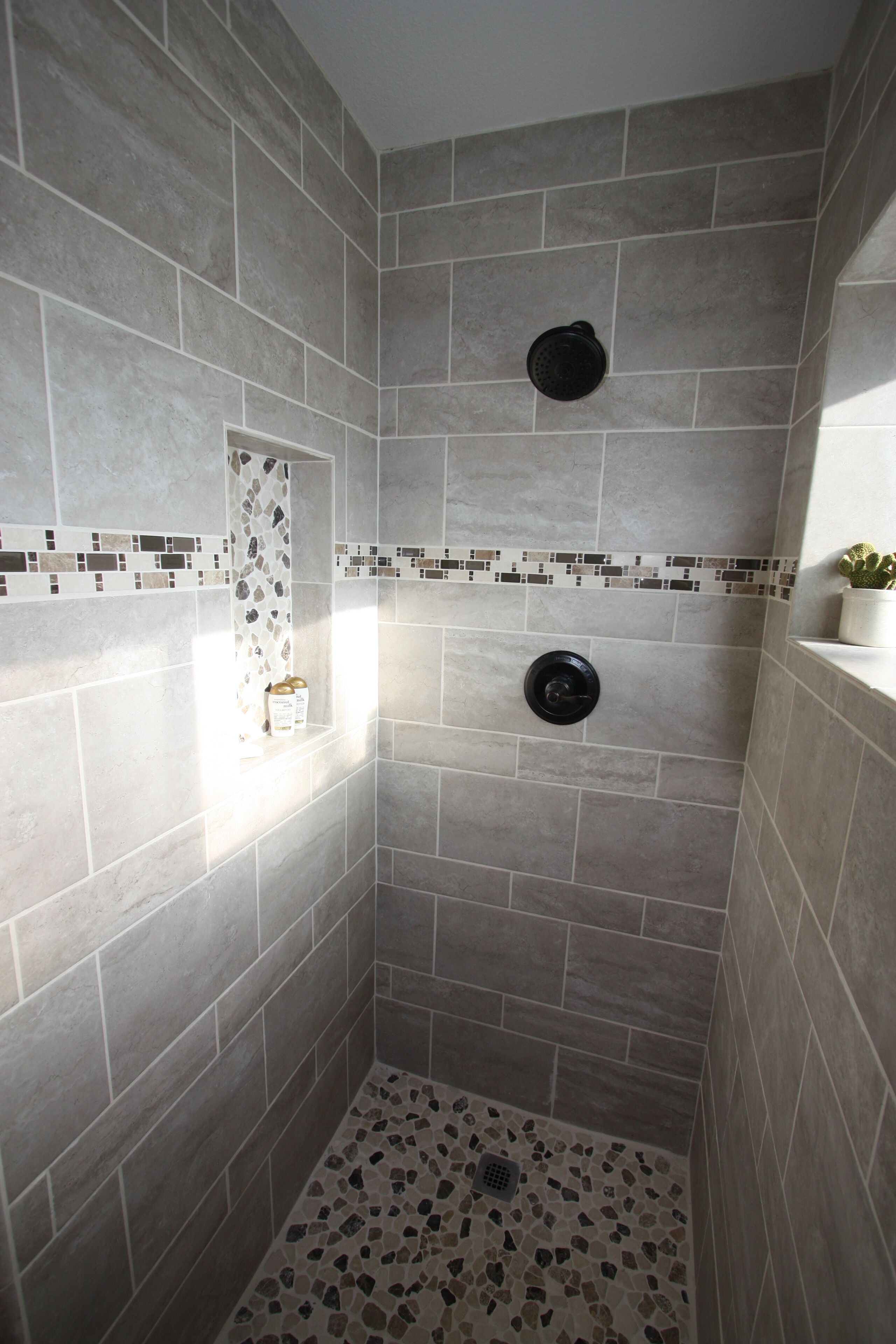 Une douche aux carreaux gris, une petite étagère avec un cactus et une bordure de mosaïque.