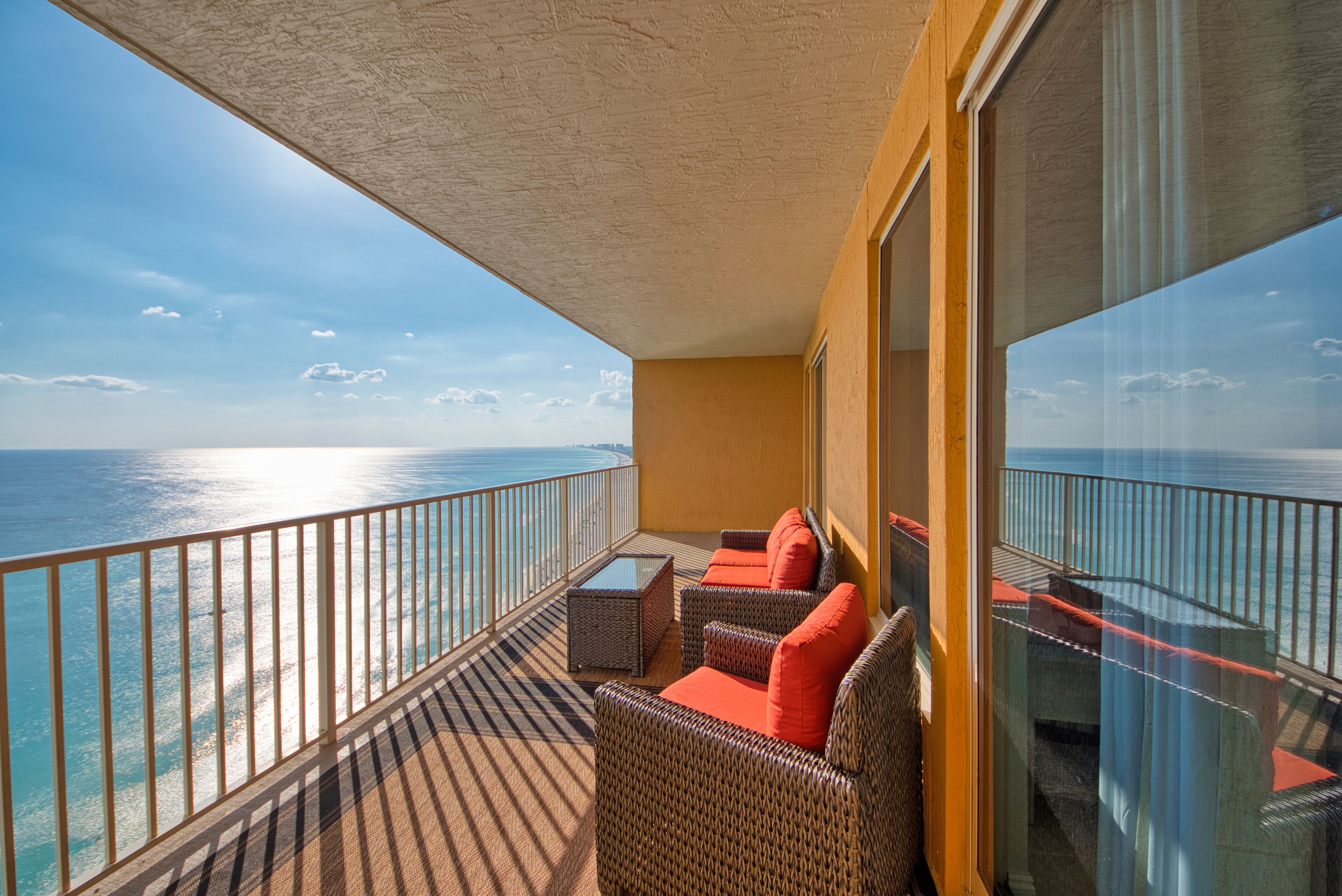 A balcony with wicker furniture and a glass railing overlooking the ocean.