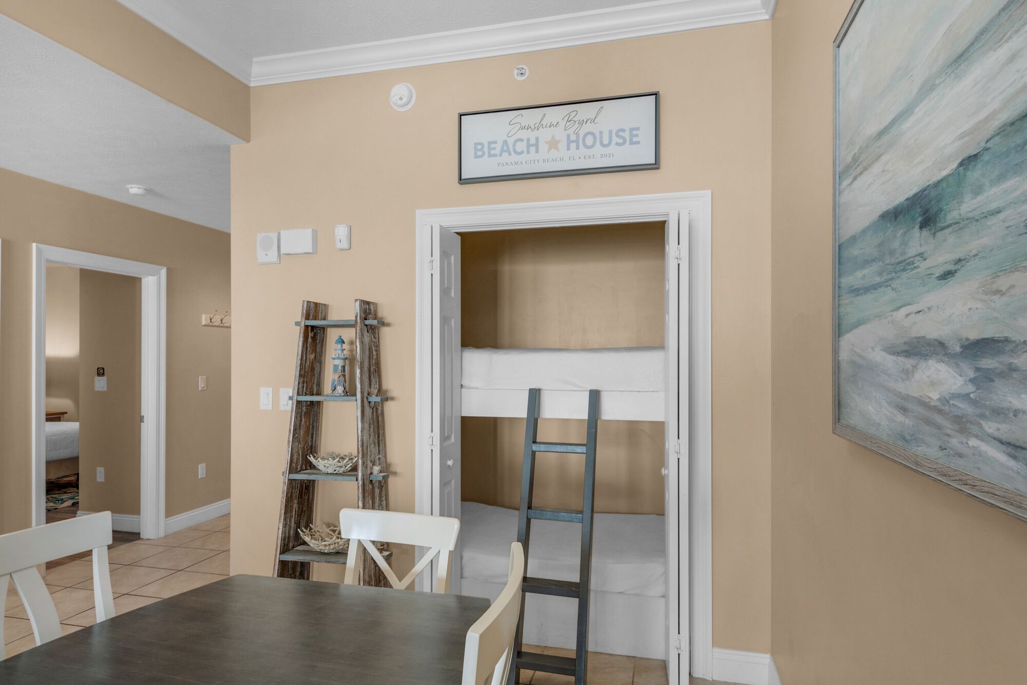 A dining area with a table and chairs, a ladder leading to a loft, and a painting on the wall.
