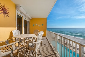 A balcony with a pool, wooden chairs, and a view of the ocean.