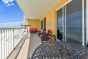 A balcony with a view of the beach, a table, chairs, and a sofa.