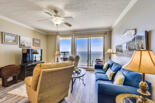 A living room with a television, a sofa, a chair, and a balcony with a view.
