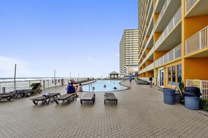 A pool area with lounge chairs and a building with balconies.