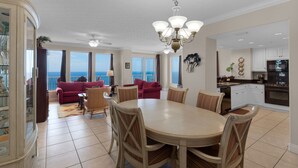 Een ruime woonkamer met een eettafel en stoelen, een balkon met uitzicht op de oceaan en een keuken met moderne apparatuur.