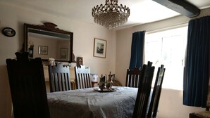 Une salle à manger avec une grande table, des chaises, un lustre et une fenêtre avec des rideaux.