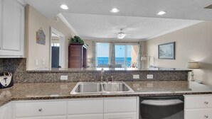 A kitchen with granite countertops, white cabinets, a double sink, and a view of the ocean through large sliding doors.