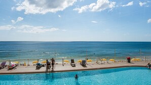 A swimming pool with a view of the ocean, sun loungers, and umbrellas.