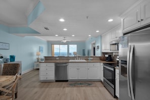 A modern kitchen with white cabinets, stainless steel appliances, and a view to the outside.