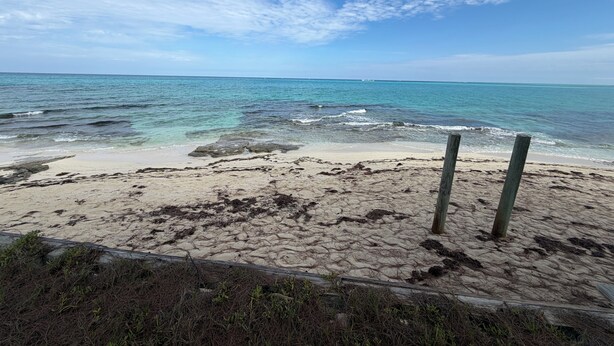 A beach with clear water, a sandy shore, and a wooden fence.