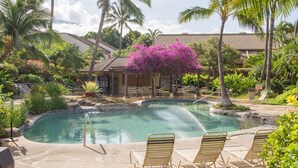 A pool area with lounge chairs, palm trees, and a building in the background.