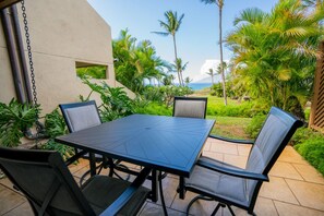 An outdoor patio with a table and chairs, surrounded by lush greenery and palm trees, overlooking a scenic view.