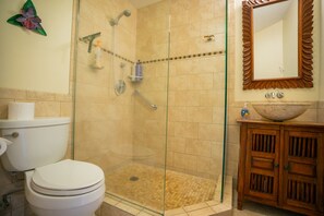 A bathroom with a glass-enclosed shower, a toilet, a sink, and a wooden cabinet.