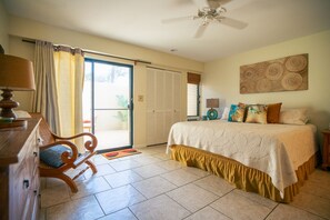 A bedroom with a bed, a chair, a dresser, a ceiling fan, and a sliding glass door leading to a balcony.