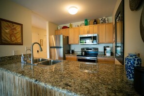 Una cocina con encimeras de granito, electrodomésticos de acero inoxidable, armarios de madera y un florero decorativo.