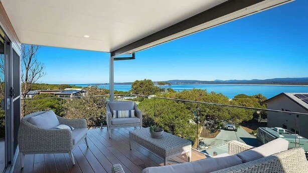 A balcony with wicker furniture, a view of the sea, and a clear sky.