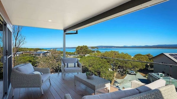 Ein Balkon mit Korbmöbeln, Blick auf das Meer und ein klarer Himmel.