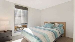 A bedroom with a bed, a nightstand, a window with a view, and a lamp.