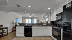 A modern kitchen with white cabinets, a black refrigerator, and a granite countertop. - 1211-12th Flr-2 Bedrooms-Sleeps 8-Outdoor Pool-Fitness Center-Hot Tub (Panama City Beach)