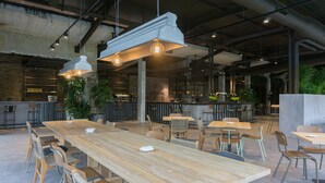 A spacious indoor dining area with long wooden tables and chairs, hanging pendant lights, and a bar area in the background. - Hostel Monte Do Gozo (Santiago de Compostela)