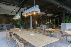Un amplio comedor interior con largas mesas y sillas de madera, lámparas colgantes y una zona de bar al fondo.