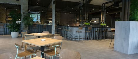A modern cafe with wooden tables and chairs, a bar area, and potted plants.