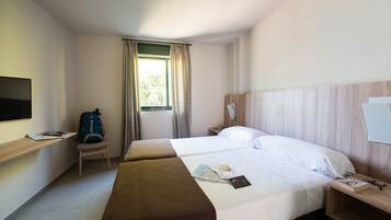 Habitación de hotel con dos camas, televisión, escritorio y ventana con cortinas.