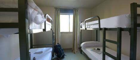 A dormitory room with bunk beds, a window with curtains, and a backpack on the floor.