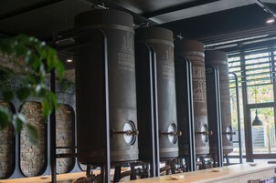 Fila de tanques cilíndricos de gran tamaño en un entorno industrial moderno, con una barra de madera y pared de piedra.