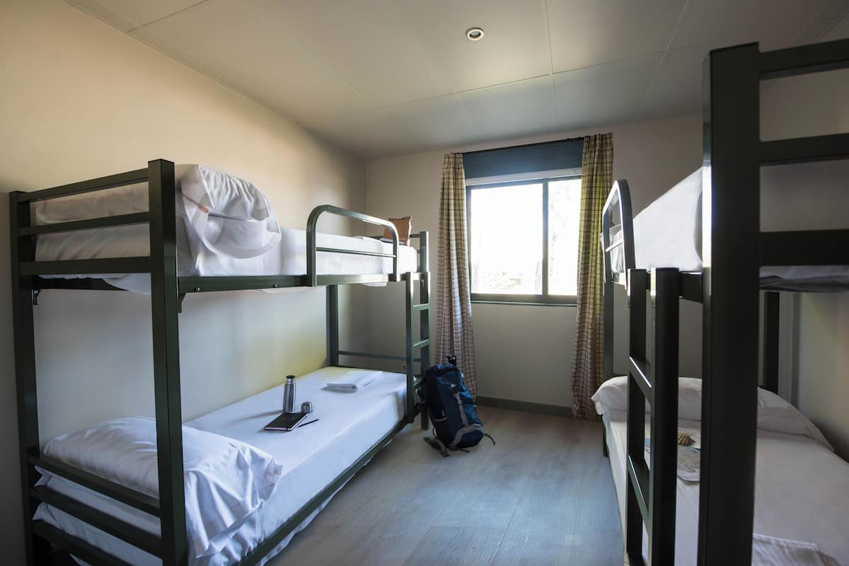 Ein Schlafsaalzimmer mit Etagenbetten, einem Fenster mit Vorhängen und einem Rucksack auf dem Boden.