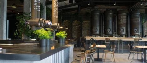 A bar area with a counter, stools, and large beer tanks in the background.