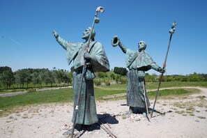 Dos estatuas de bronce de hombres con los brazos levantados e instrumentos musicales en un campo abierto.