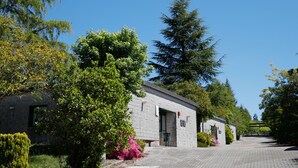 A stone building with a door and windows, surrounded by trees and shrubs. - Hostel Monte Do Gozo (Santiago de Compostela)