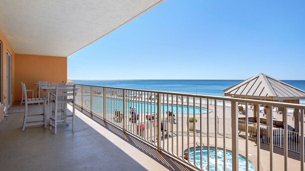 A balcony with a view of the ocean, a pool, and outdoor seating.