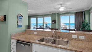 A kitchen with granite countertops, stainless steel sink, and white cabinets. There is a view of the ocean through large windows.
