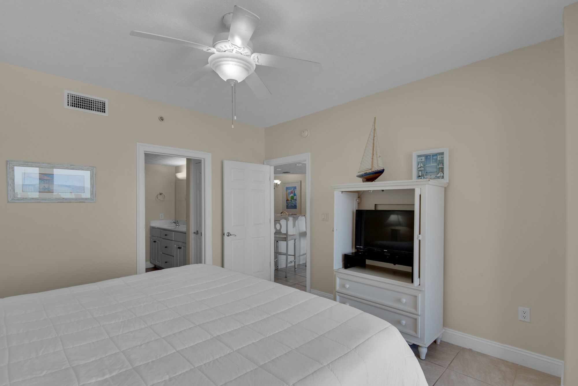 A bedroom with a bed, a ceiling fan, a TV, and a small sailboat decoration.