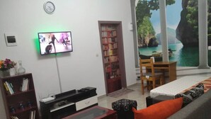 A living room with a television, bookshelf, sofa, and a view of a scenic landscape through a window.