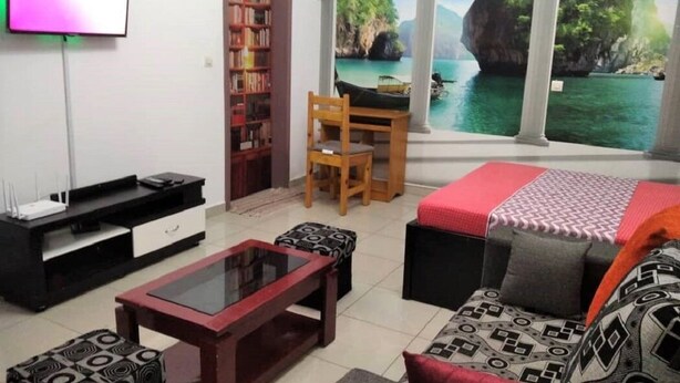 A living room with a TV, a bookshelf, a desk, a sofa, and a window with a scenic view.