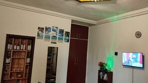 A room with a bookshelf, a cabinet, a wall-mounted TV, and a decorative light.