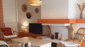 A modern living room with a flat-screen TV, wicker furniture, and decorative wall art. - The Clairette de Gascogne, space and comfort (CONDOM)
