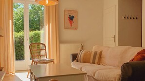 A cozy living room with a white sofa, a wooden chair, a table, and a woven ottoman. - The Clairette de Gascogne, space and comfort (CONDOM)