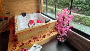 A modern bathroom with a wooden floor, a large bathtub, and a view of a forest through large windows. - Hira Bungalov (Camlihemsin)