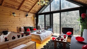 A wooden cabin with a large bed, a wooden bench, a dining table, and a view of the forest through large windows. - Hira Bungalov (Camlihemsin)