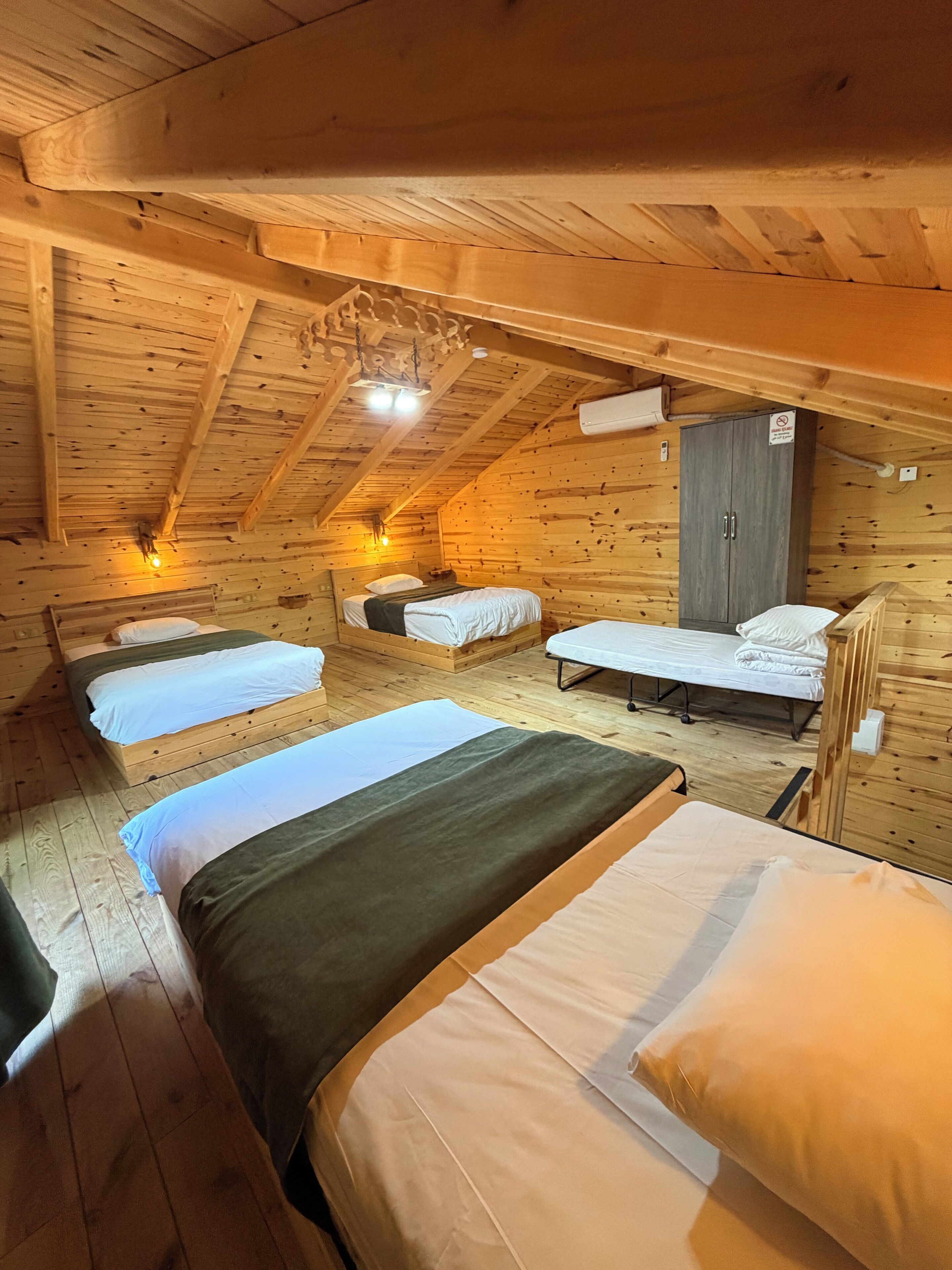 A cabin with four beds arranged in a U-shape, wooden walls, a wooden ceiling, and a small wardrobe.
